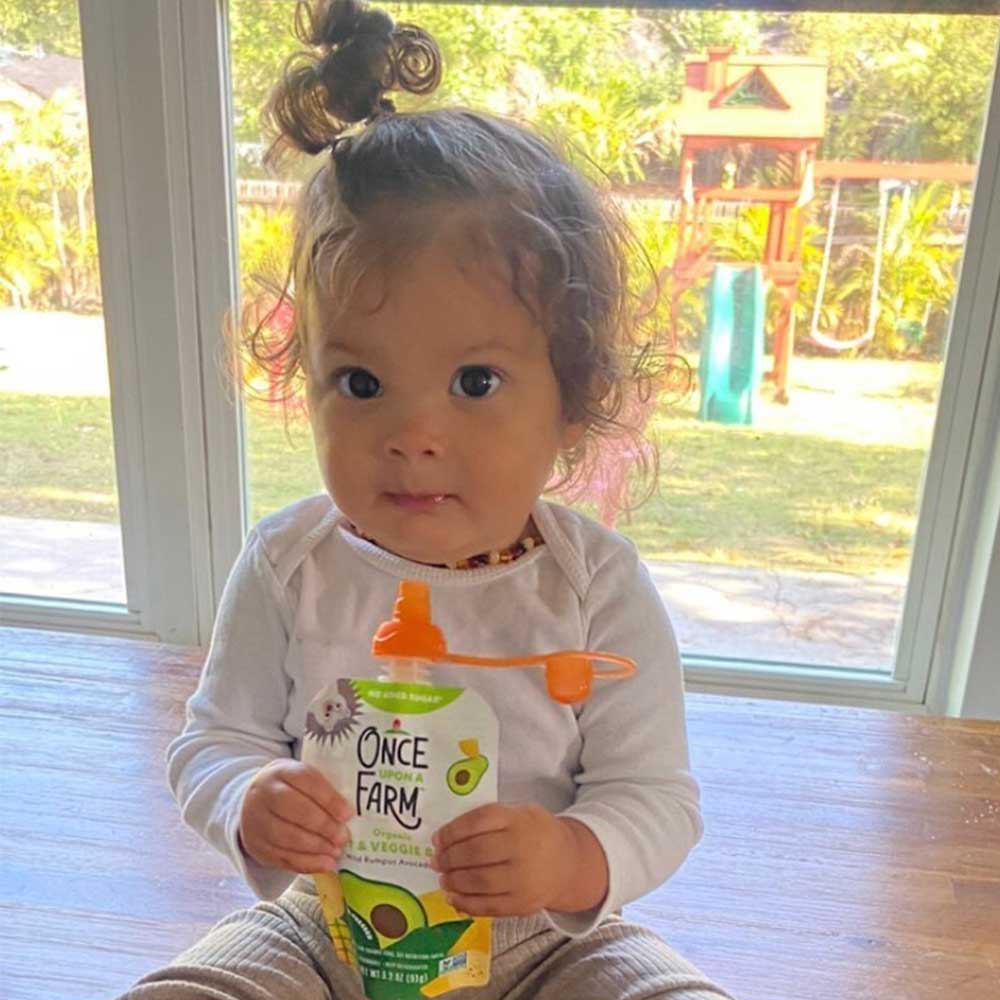 A picture of a toddler inside the house holding a pouch with an orange ChooMee Pouch Topper.