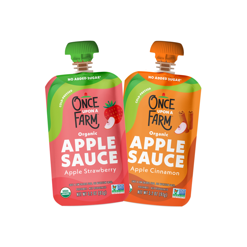 Two pouches of Once Upon a Farm Organic Apple Sauce are shown side by side on a plain white background. The left pouch is Apple Strawberry with a green cap and pink-red label, and the right pouch is Apple Cinnamon with an orange cap and orange label.