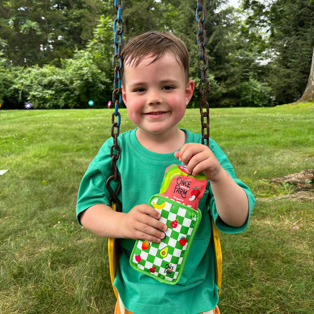 Child on a swing holding a pouch cooler with Once Upon a Farm Strawberry Applesauce pouch